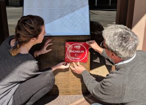 Carla Carreras i Pere Miquel Carreras penjant la placa que indica que Les Corones és un establiment recomanat a la Guia Michelin 2018.