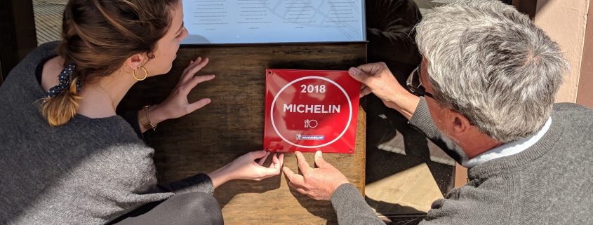 Carla Carreras i Pere Miquel Carreras penjant la placa que indica que Les Corones és un establiment recomanat a la Guia Michelin 2018.
